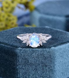 an oval shaped blue topazte and diamond ring on a velvet box with flowers in the background