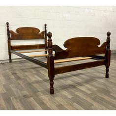 a wooden bed frame sitting on top of a hard wood floor next to a white brick wall