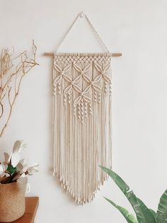 a white wall hanging next to a potted plant