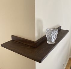 a glass vase sitting on top of a wooden shelf next to a white painted wall