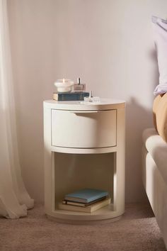 a white nightstand with a blue book on it next to a bed in a bedroom