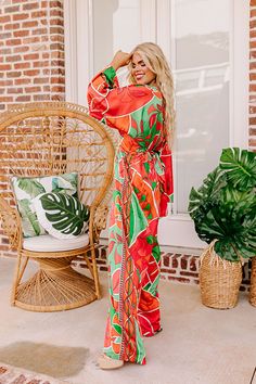 - This stunning jumpsuit is a ticket to sunshine vibes! Featuring a bold vibrant print and a chic satin finish, this trendy wide leg jumpsuit promises to steal the spotlight and keep you feeling fabulous. - Unlined material with a pink, orange, and green hued abstract botanical print with a satin finish - A v-cut neckline and a v-cut back with a tie detail - Long. loose sleeves - A waistline with an elastic back and an attached tie closure belt - A relaxed silhouette that ends in wide hemlines Chic Orange Jumpsuits And Rompers For Vacation, Chic Orange Jumpsuit And Romper For Vacation, Tropical Multicolor Jumpsuits And Rompers For Day Out, Trendy Orange Jumpsuits And Rompers For Beach, Multicolor Maxi Length Jumpsuits And Rompers For Vacation, Multicolor Printed Maxi-length Jumpsuits And Rompers, Orange Floral Print Jumpsuit For Beach, Orange Floral Print Jumpsuit For Vacation, Orange Floral Print Jumpsuits And Rompers For Vacation