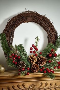 a wreath with pine cones and berries on top of a fireplace mantel in front of a white wall