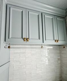 a kitchen with gray cabinets and white subway tile backsplash, gold pulls on the handles