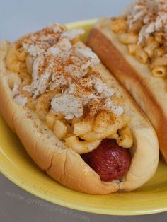 two hot dogs covered in macaroni and cheese on a yellow plate with a fork