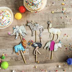 cupcakes and cake toppers are arranged on a wooden table with sprinkles