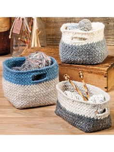 three knitted storage baskets sitting on top of a wooden table next to bottles and knitting needles