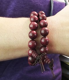 12mm Violet Wood Purpleheart wood beads strung on elastic cord fits a 6.5 inch wrist.  2mm hole. As our mala are hand-carved and assembled from natural materials, bead and tassel appearance may vary.  The beads are 12mm wide.  $12 per bracelet (our model is wearing two bracelets in the photo). Violet Wood Purpleheart meaning: Purpleheart gets its name from the color of the wood.  Its scientific name is Peltogyne.  It has other names in addition to Violet Wood and Purpleheart, such as Amendim and Spiritual Wooden Beads Stretch Bracelet For Meditation, Spiritual Stretch Bracelet With Wooden Beads For Meditation, Traditional Wood Bracelets With Round Beads, Traditional Wooden Bracelets With Round Beads, Traditional Wooden Bracelet With Round Beads, Traditional Adjustable Wooden Beads Stretch Bracelet, Adjustable Wooden Beads Rosary Bracelet For Meditation, Traditional Wooden Beaded Bracelets, Adjustable Wooden Beaded Bracelets For Meditation