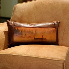 a pillow sitting on top of a chair in front of a brown couch with a painting on it