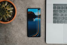 an open laptop computer sitting on top of a desk next to a plant and phone