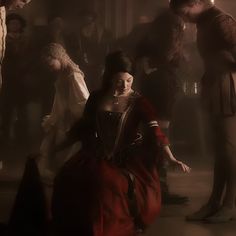 a woman in a red dress sitting on the ground with other people standing around her