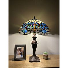 a lamp sitting on top of a wooden table next to a framed photo and potted plant