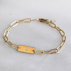 This stunning personalized bracelet is meaningful and stylish. This dainty bracelet is handmade with silver or gold chain and your initial or symbol. It makes a wonderful gift for her for any occasion. D E T A I L S *Thick 16mm bar *Paperclip chain *100% 14kt Gold-Filled JUST FOR YOU *Stamped by hand with an initial in classic block. *See our chart for available symbols. *Satin finish. LENGTH Fits most sizing: 6.0 inches extra small 6.5 inches small 7.0 inches medium 7.5 inches large HOW TO PERS Stamp Bracelet Ideas, Nickel-free Gold Name Bracelet For Everyday, Nickel-free Gold Link Bracelets, Modern Personalized Metal Jewelry, Gold Charm Bracelet With Chain As A Gift, Gift Link Chain Bracelet, Personalized 14k Gold Link Jewelry, Classic Gold Bracelets For Friendship, Modern Personalized Jewelry For Friendship