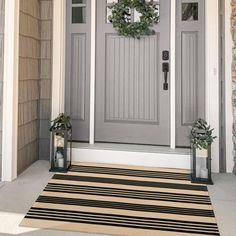 a gray front door with two wreaths on it and a black and white striped rug