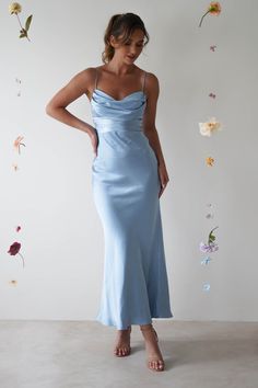 a woman wearing a blue dress standing in front of a wall with flowers on it