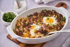 a casserole dish with eggs and meat in it on a wooden cutting board