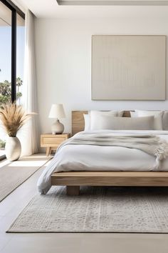 a large white bed sitting in a bedroom next to a tall glass window on top of a hard wood floor