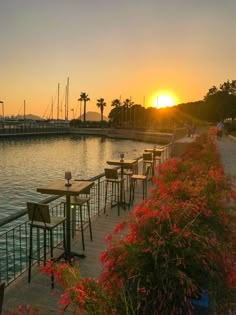 the sun is setting over some water with tables and chairs