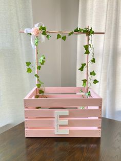 a pink wooden box with ivy and flowers on it, sitting on a wood table