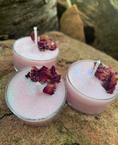 three candles with flowers in them sitting on a rock