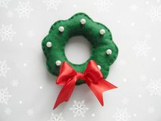 a green wreath with red ribbon and white balls on it sitting next to snowflakes