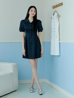 a woman standing in front of a white couch next to a coat rack with clothes hanging on it