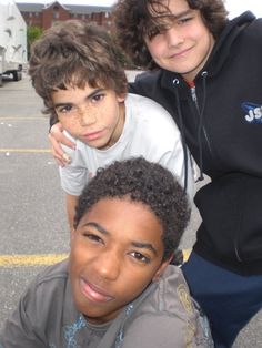 three young boys posing for a photo in a parking lot with their arms around each other