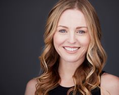 a woman with blonde hair and blue eyes smiling at the camera while wearing a black top