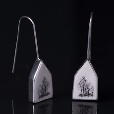 two silver earrings with trees on them sitting on top of a black table next to each other