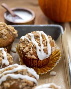 muffins with white icing sitting on a tray next to some pumpkins