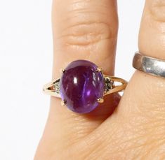 a woman's hand holding a ring with an oval shaped purple stone on it