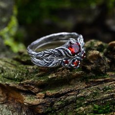 a silver ring with red stones on top of a tree branch in the woods,