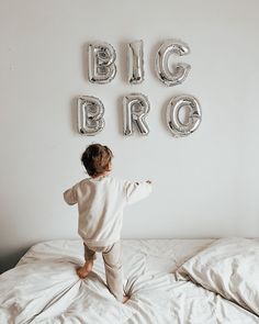 a little boy standing on top of a bed in front of balloons that spell out the word big bro