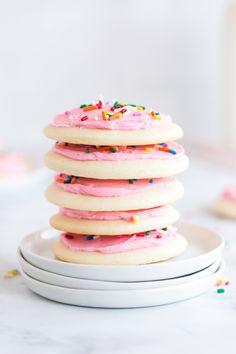 a stack of cookies with pink frosting and sprinkles on top sitting on plates