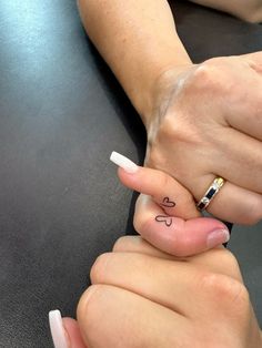 two people holding hands with tattoos on their fingers, one has a heart and the other has a love