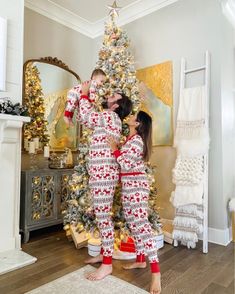 a man and woman in matching pajamas standing next to a christmas tree