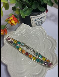 a white plate with a colorful bracelet on it next to a potted plant and some flowers