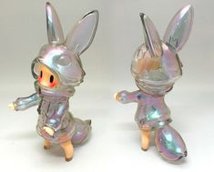 two glass figurines are shown in the shape of rabbits, one is wearing a silver outfit and the other has an orange nose