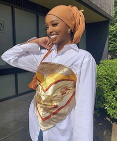 a woman wearing a white shirt and orange head scarf is standing in front of a building