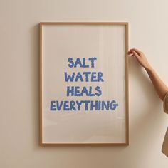 a woman holding up a framed poster with the words salt water heals everything