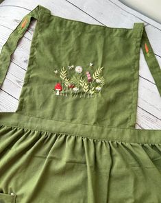 a green apron with embroidered flowers and plants on the front, sitting on a white wooden table