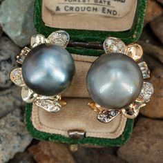 These gorgeous pearl earrings are each accented with one (1), post set, cultured Tahitian pearl, eleven (11), bead set, round brilliant cut diamonds and two (2), prong set, baguette cut diamonds. The earrings measure 22.8mm X 17.3mm. The earrings are finished with hinged omega backs for pierced ears. One of the baguette diamonds is unnoticeably chipped. Tahitian Pearl Jewelry With Diamond Accents For Wedding, Fine Jewelry Tahitian Pearl For Wedding, Tahitian Pearl Fine Jewelry For Wedding, Tahitian Pearl Jewelry With Matching Earrings For Anniversary, Classic Tahitian Pearl Jewelry With Matching Earrings, Elegant Tahitian Pearl Earrings For Wedding, Tahitian Pearl Round Earrings For Wedding, Round Tahitian Pearl Earrings For Wedding, Luxury Tahitian Pearl Wedding Earrings