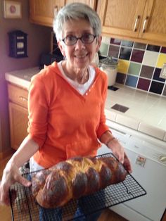 an older woman holding a loaf of bread on top of a rack in the kitchen