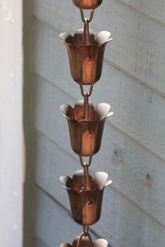 three tiered metal vases are hanging from the side of a building with white siding behind them