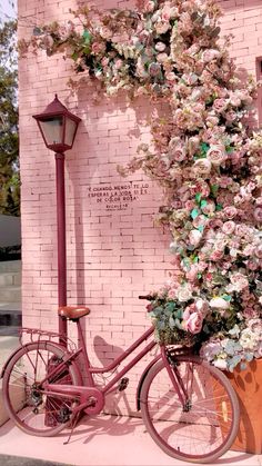 a bicycle parked next to a pink brick wall with flowers growing on it's side