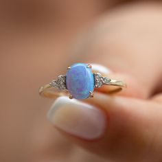 a woman holding an opal and diamond ring in her hand