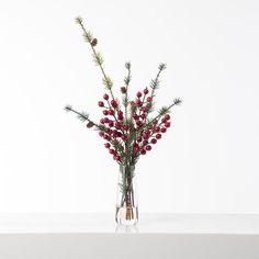 a glass vase filled with red berries and pine cones on top of a white table