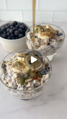 two bowls filled with oatmeal sitting on top of a counter next to blueberries