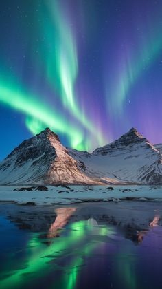 the northern lights shine brightly over snow covered mountains and water in this landscape photo taken at night