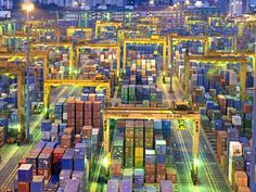 an aerial view of shipping containers in a large container yard at night, with city lights on the horizon